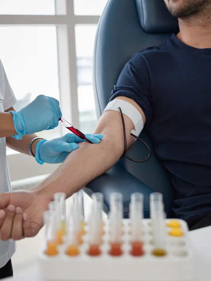 A lab technician in gloves taking a routine blood sample from a man’s arm