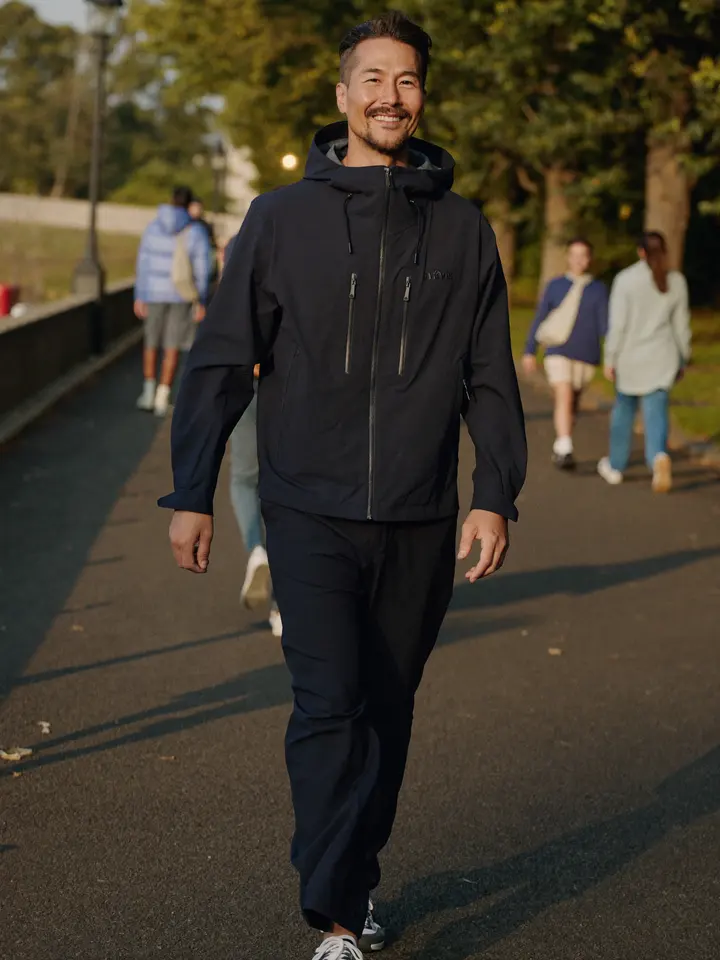 A smiling man walking along a tree-lined park path at golden hour