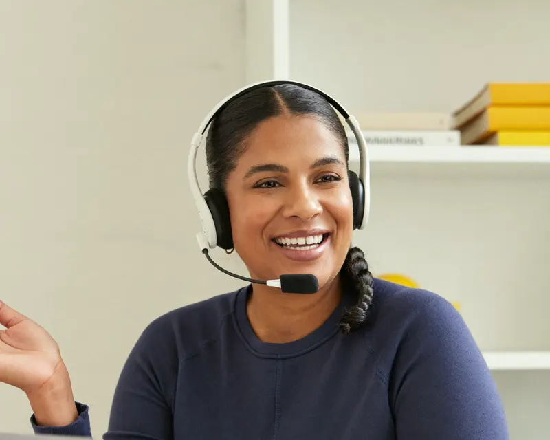A wellness coach with a headset smiling during a video call at her desk